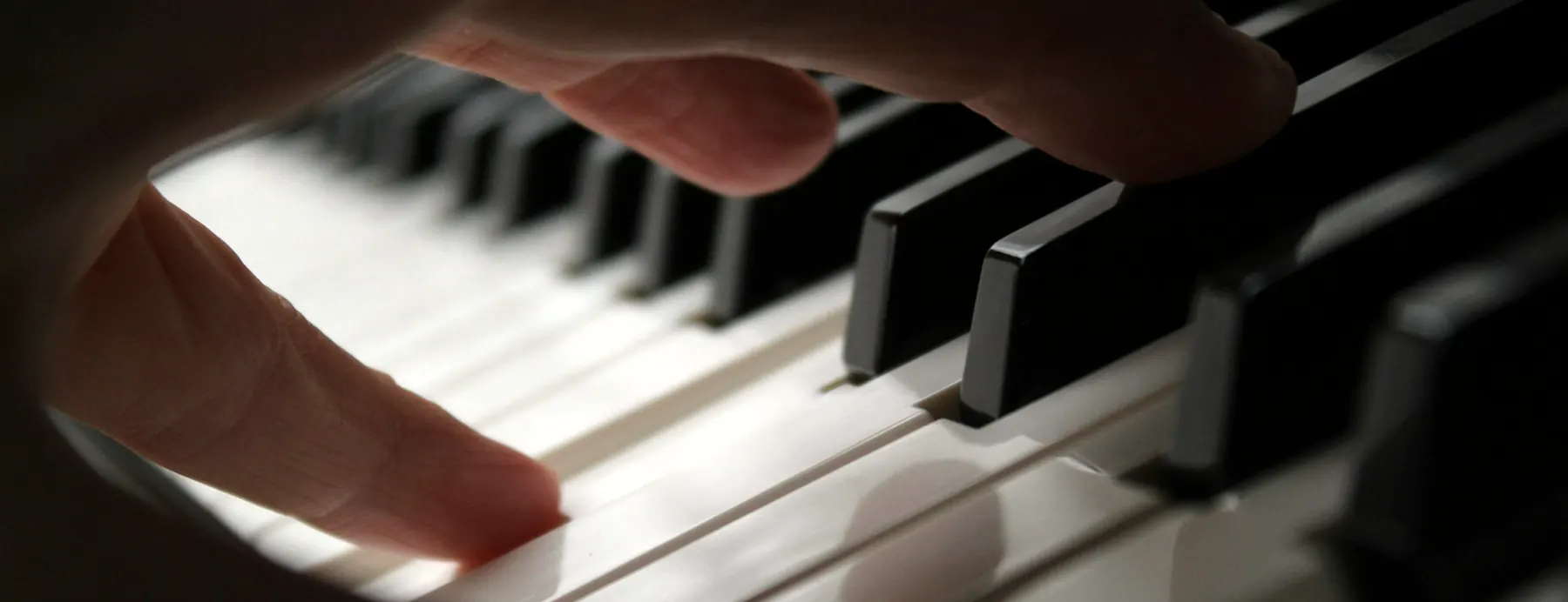 Doigts qui effleurent les touches d’un piano dans une lumière douce